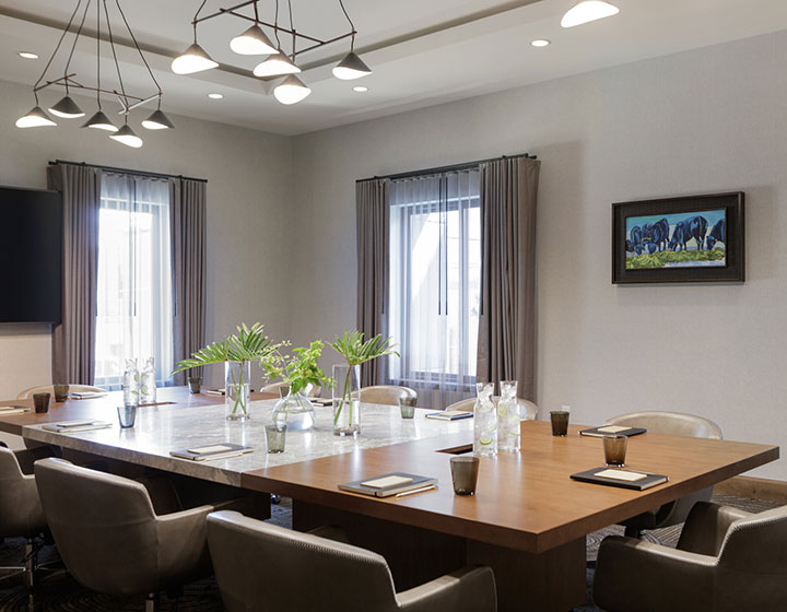 Meeting boardroom with meeting table setup of water, pens, notebooks, chairs, and flowers